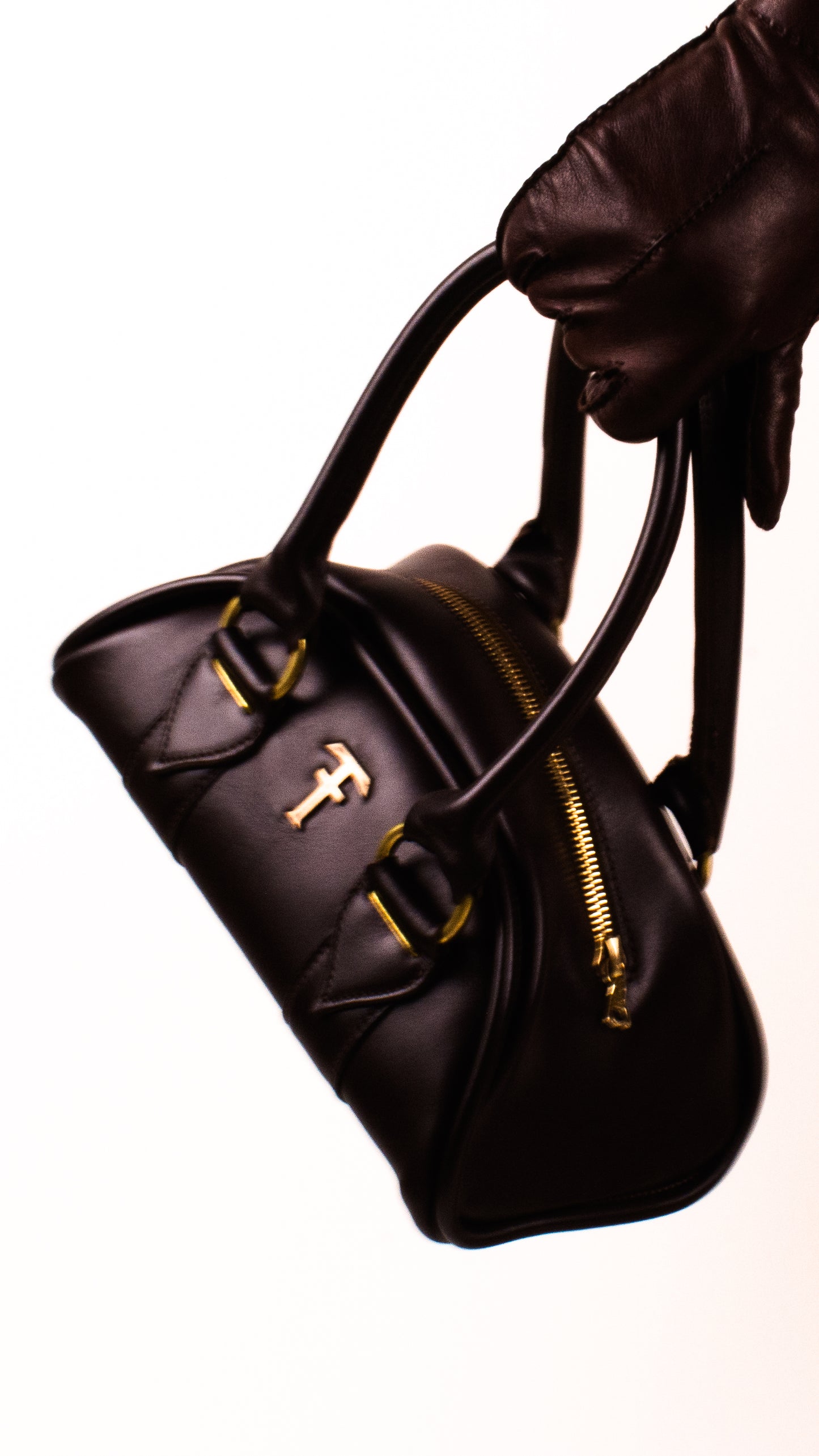 Black handbag with Bronze Tough Auto  accents held by a gloved hand on a white background