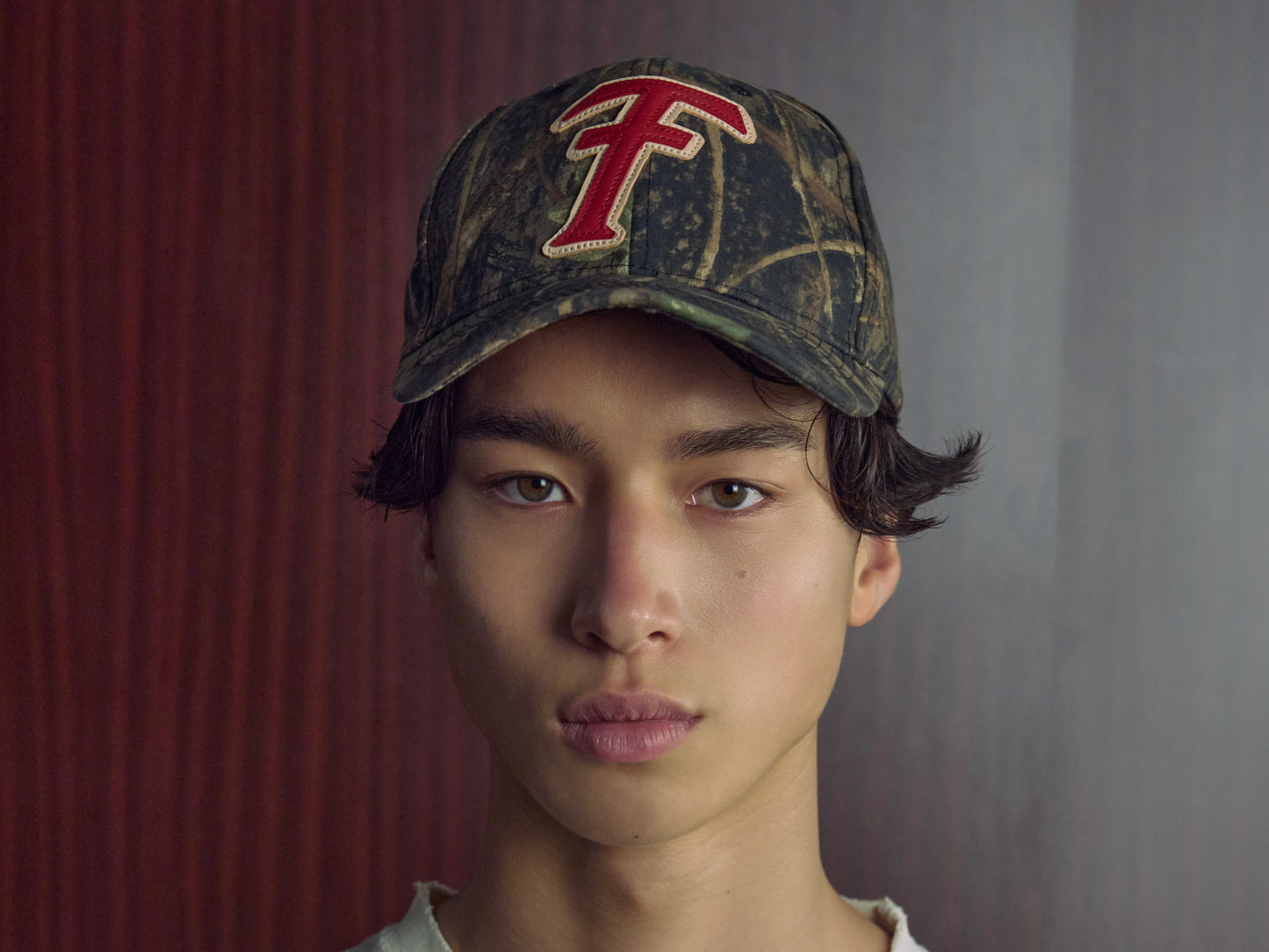 Person wearing a camouflage cap with a red logo on a plain background