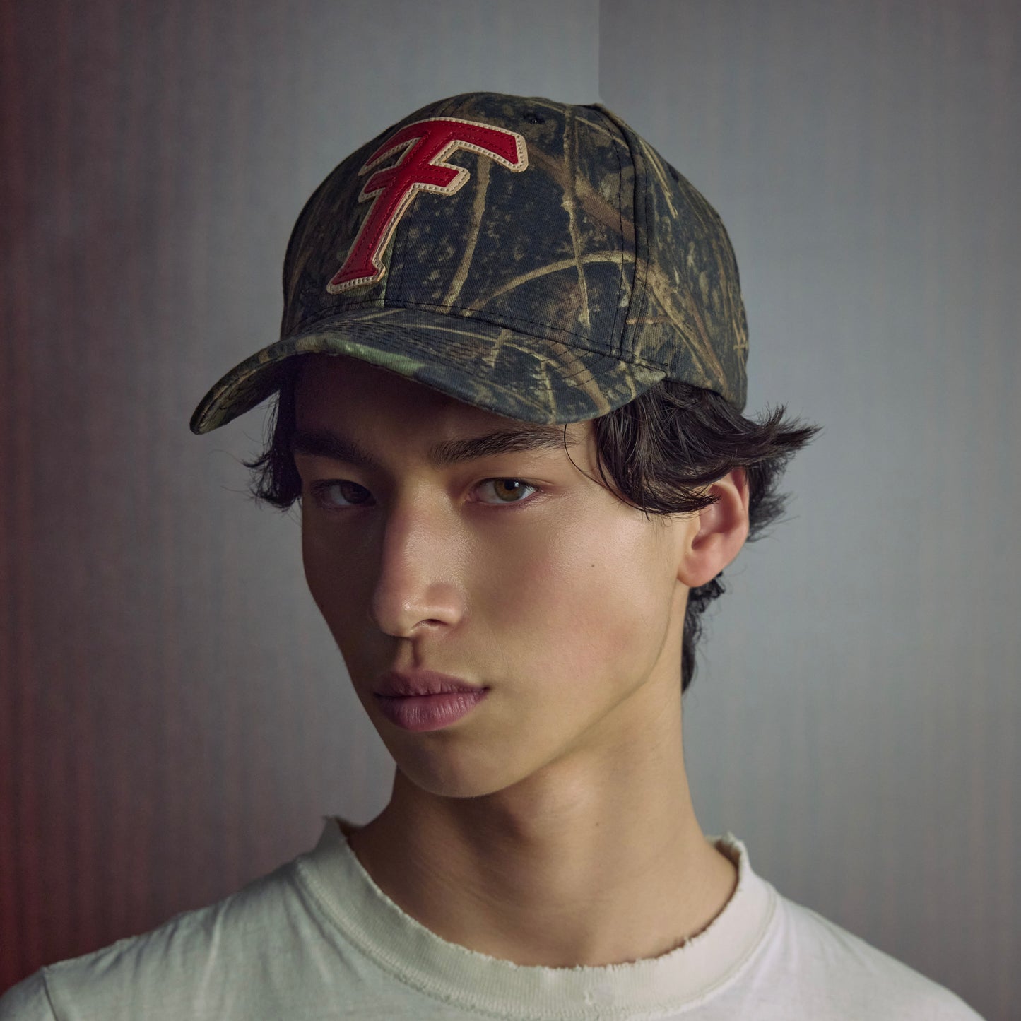 Person wearing a camouflage cap with a red logo on a gray background