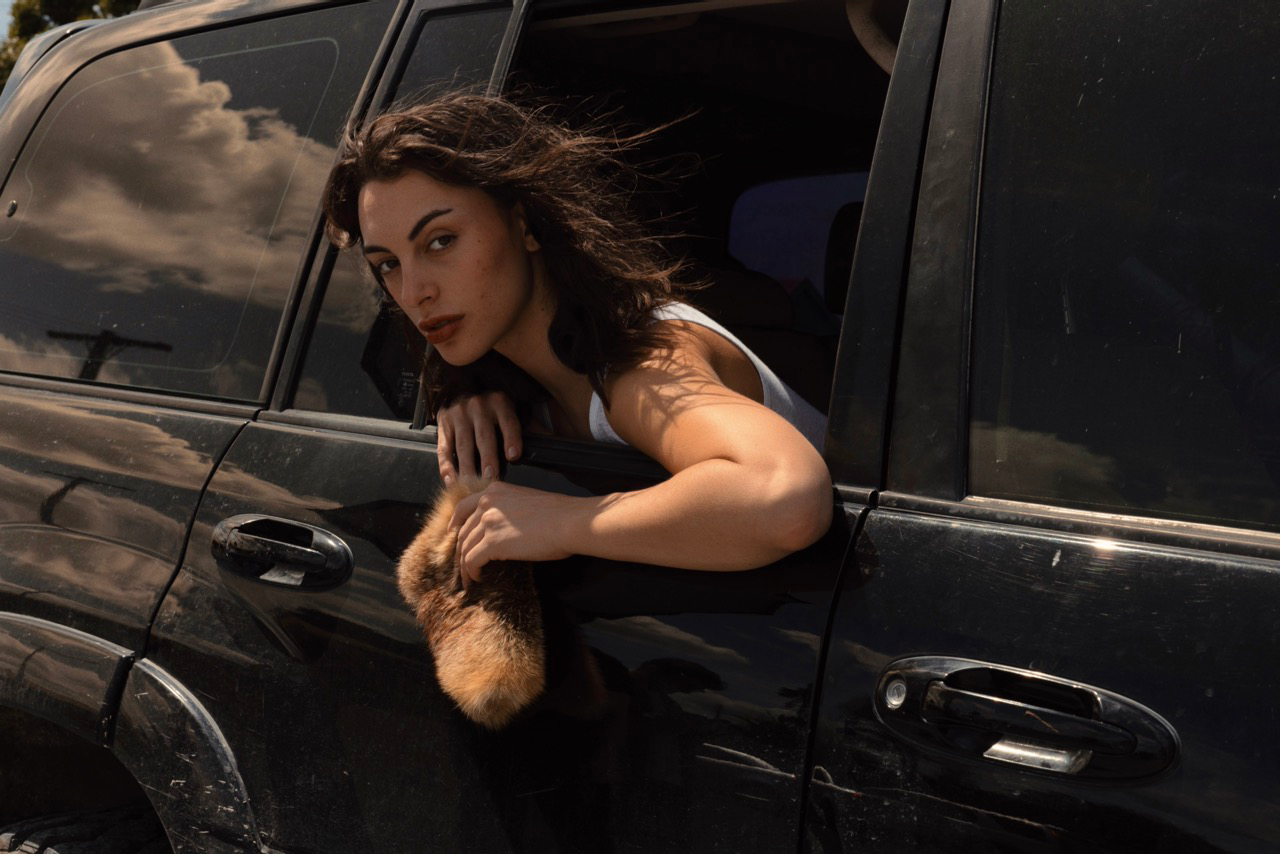 Woman leaning out of a car window with a fur purse , surrounded by dark tones.
