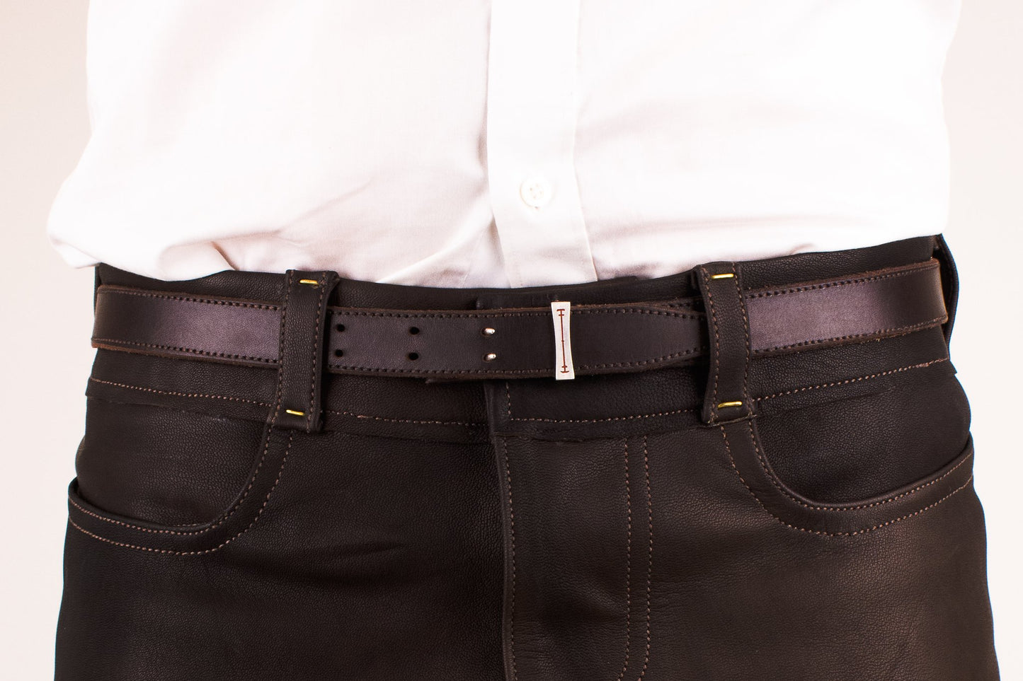 Person wearing brown pants with a belt on a plain background
